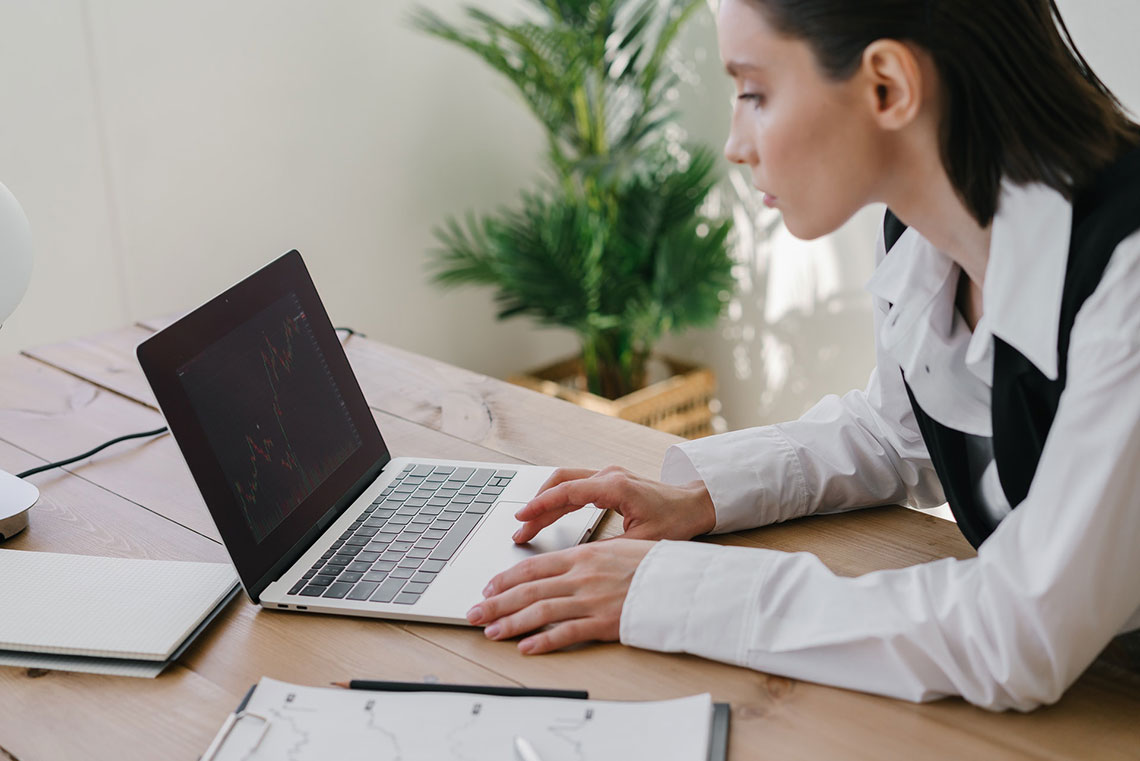 A businesswoman in a white shirt and black vest searches on a laptop computer