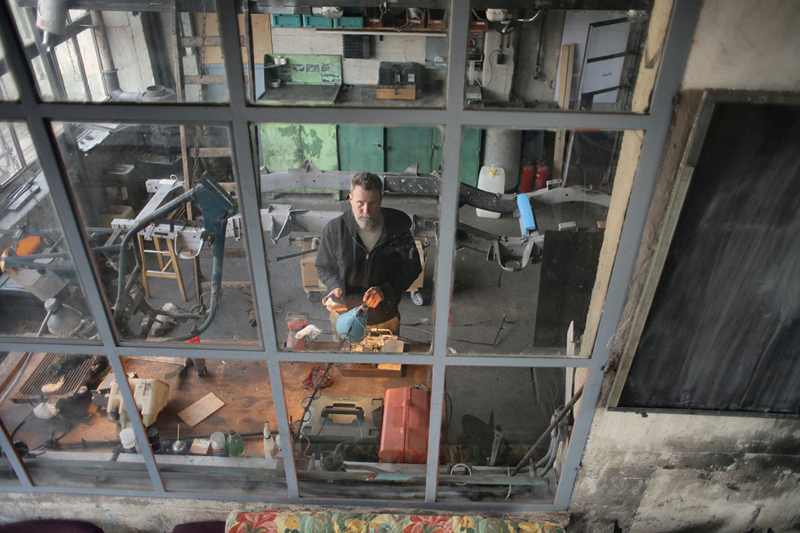 man using various tools and equipment, seen from outside his studio window