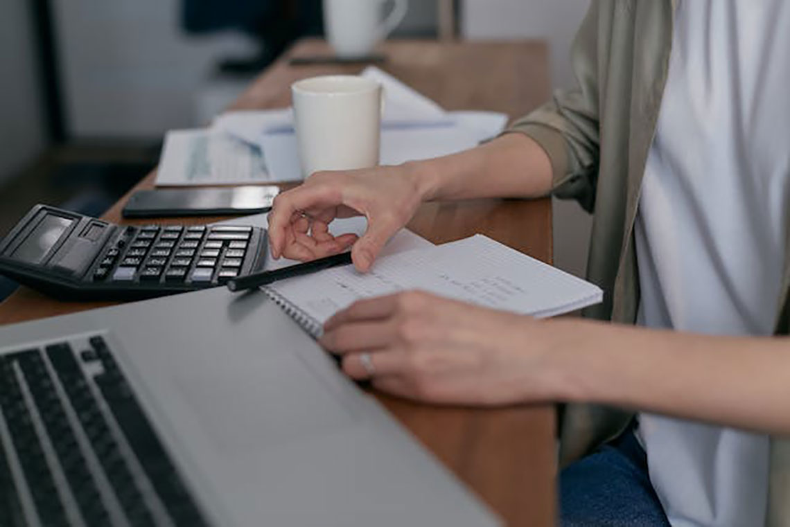 close up of hands typing while calculating debts manually in a ledger