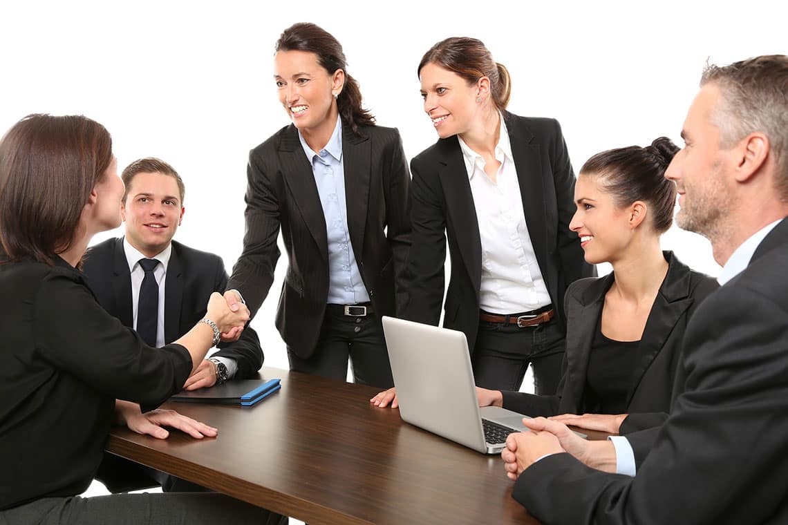 Business professionals in formal attire shaking hands and collaborating around a wooden meeting table